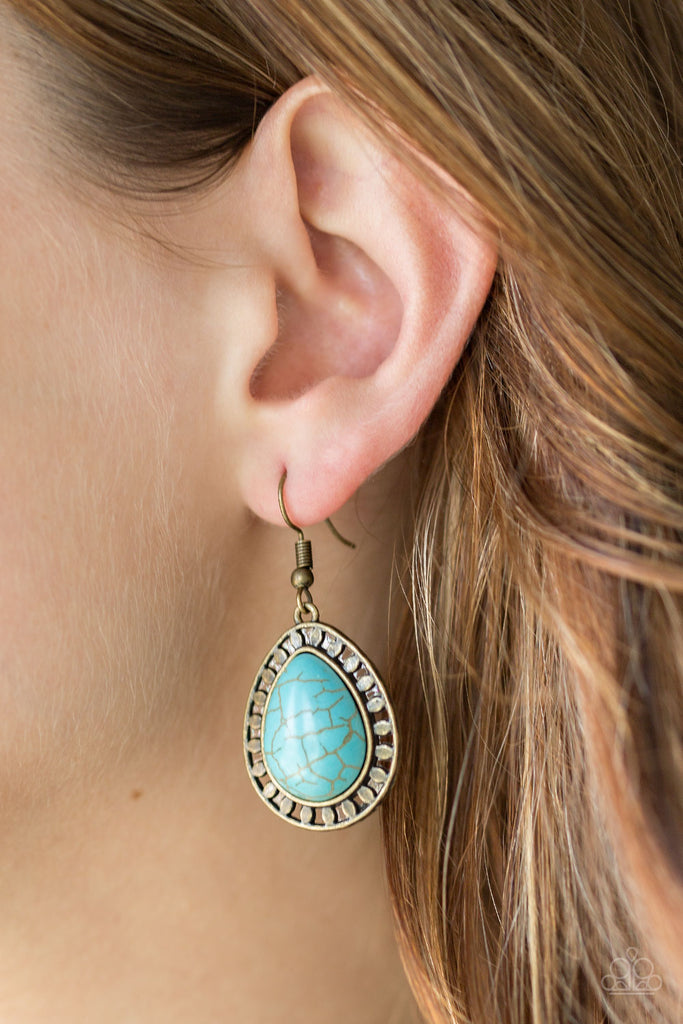 Chiseled into a tranquil teardrop, a refreshing turquoise stone is pressed into a shimmery brass frame radiating with tribal inspired textures for a seasonal look. Earring attaches to a standard fishhook fitting.  Sold as one pair of earrings.