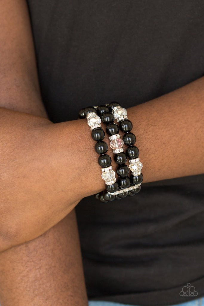 Pinched between white rhinestone encrusted frames, white rhinestone encrusted rings, crystal-beads, and shiny black beads are threaded along elastic stretchy bands for a glamorous look.  Sold as one individual bracelet.