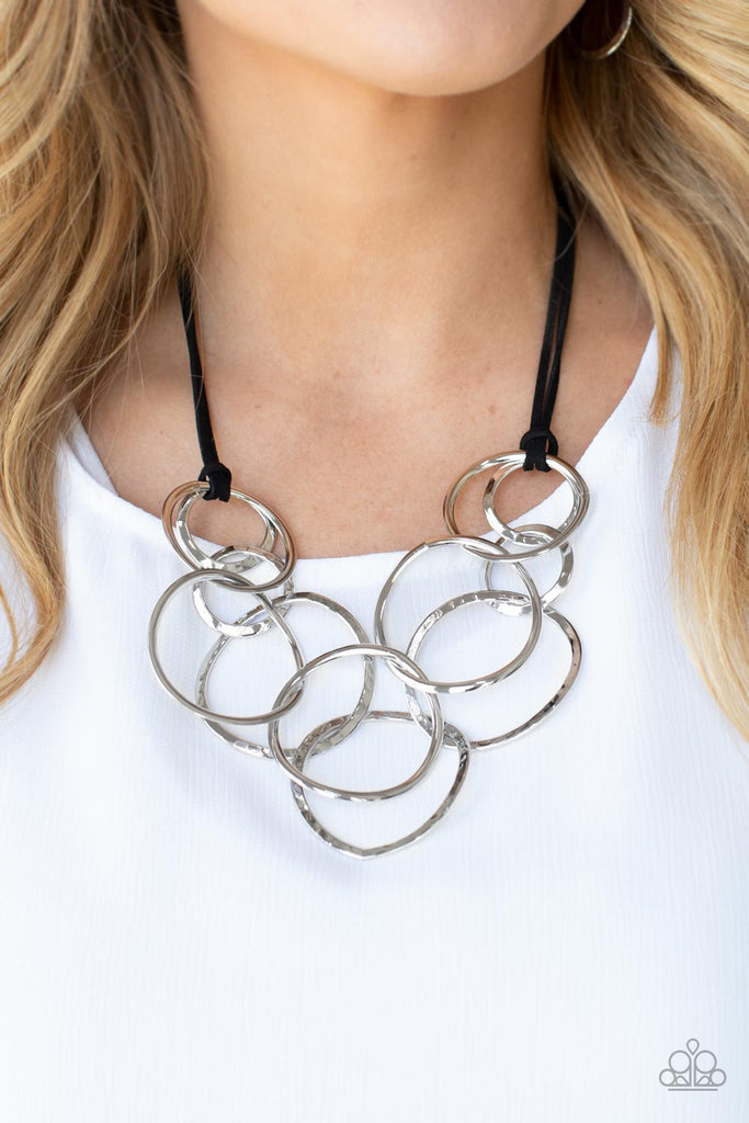 Black suede cords knot around a mismatched assortment of hammered silver rings that interlock below the collar, creating two rows of dizzying texture. Features an adjustable clasp closure.  Sold as one individual necklace. Includes one pair of matching earrings.