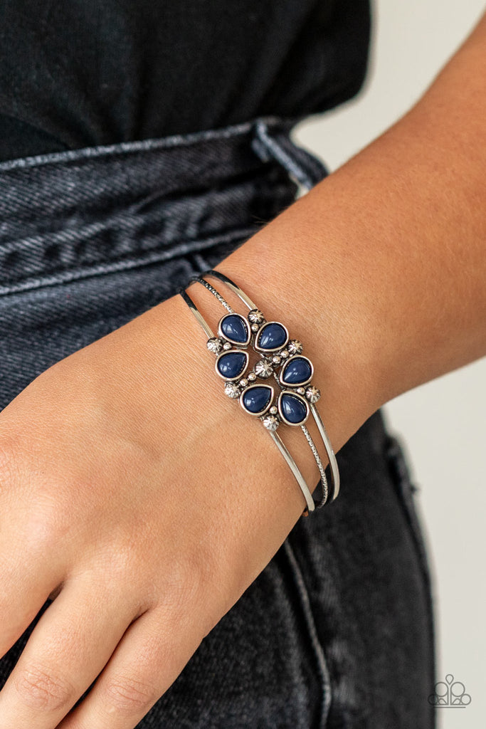 A whimsical collection of glassy blue teardrop beads, dainty silver studs, and silver floral accents coalesce into a colorful centerpiece atop a layered silver cuff.  Sold as one individual bracelet.