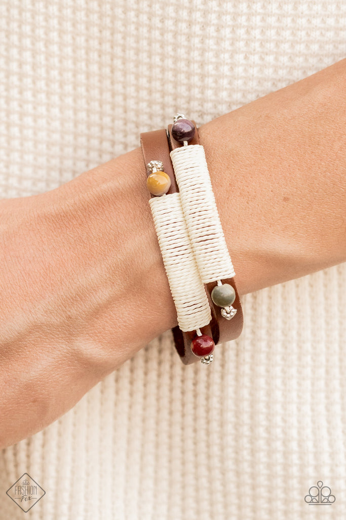 Layered brown leather bands are wrapped with natural creme-colored cording and adorned at each end with an earthy multicolored stone and dainty silver accents, resulting in a rustic homespun finish as it wraps around the wrist. Features an adjustable snap closure.  Sold as one individual bracelet.
