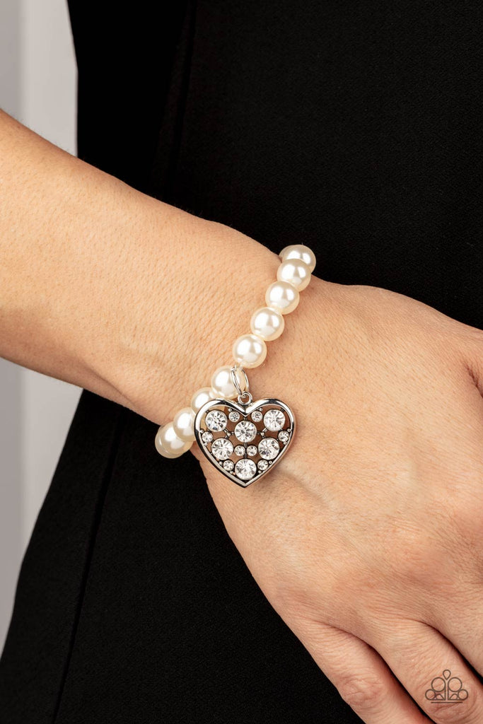 A dramatically oversized white rhinestone encrusted silver heart charm dangles from a stretchy strand of bubbly white pearls, creating a flirtatious dazzle.  Sold as one individual bracelet.
