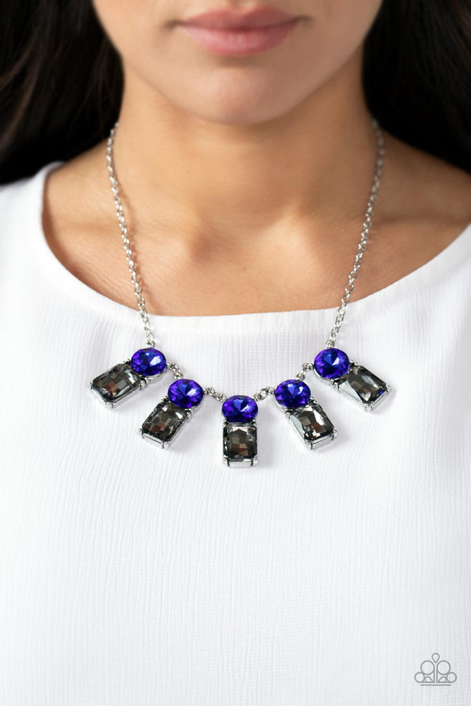 A sparkly row of oversized blue gems regally sit atop emerald cut smoky rhinestone bases as they delicately link along a dainty silver chain below the collar, resulting in a royal glamorous centerpiece. Features an adjustable clasp closure.  Sold as one individual necklace. Includes one pair of matching earrings.