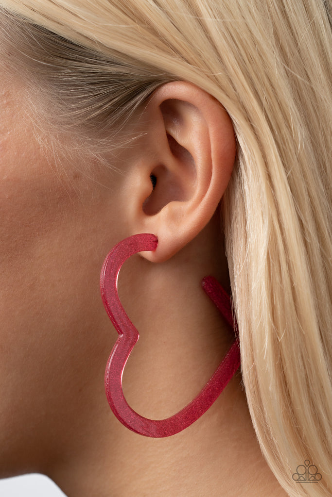 Dusted in sparkles, a pink acrylic frame delicately curls into a flat heart frame for a flirtatious finish. Earring attaches to a standard post fitting. Hoop measures approximately 2 1/2" in diameter.  Sold as one pair of hoop earrings.