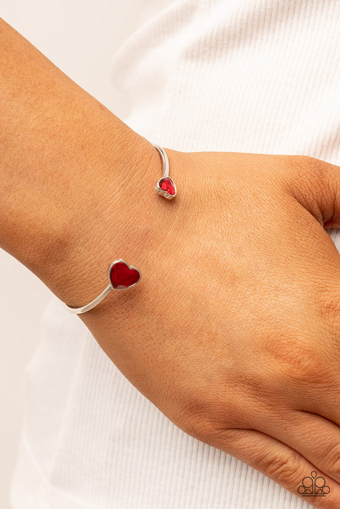 Enhanced with glitzy red rhinestones, two silver hearts adorn the ends of a silver band that curls around the wrist for a flirtatious open-faced style cuff.  Sold as one individual bracelet.