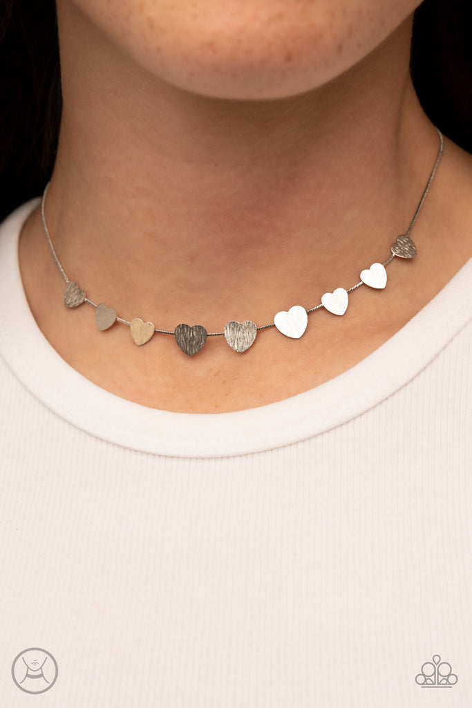 Delicately scratched in shimmer, a dainty collection of flat silver heart frames gradually increases in size along a shiny silver snake chain around the neck for a flirtatious fashion. Features an adjustable clasp closure.  Sold as one individual choker necklace. Includes one pair of matching earrings.