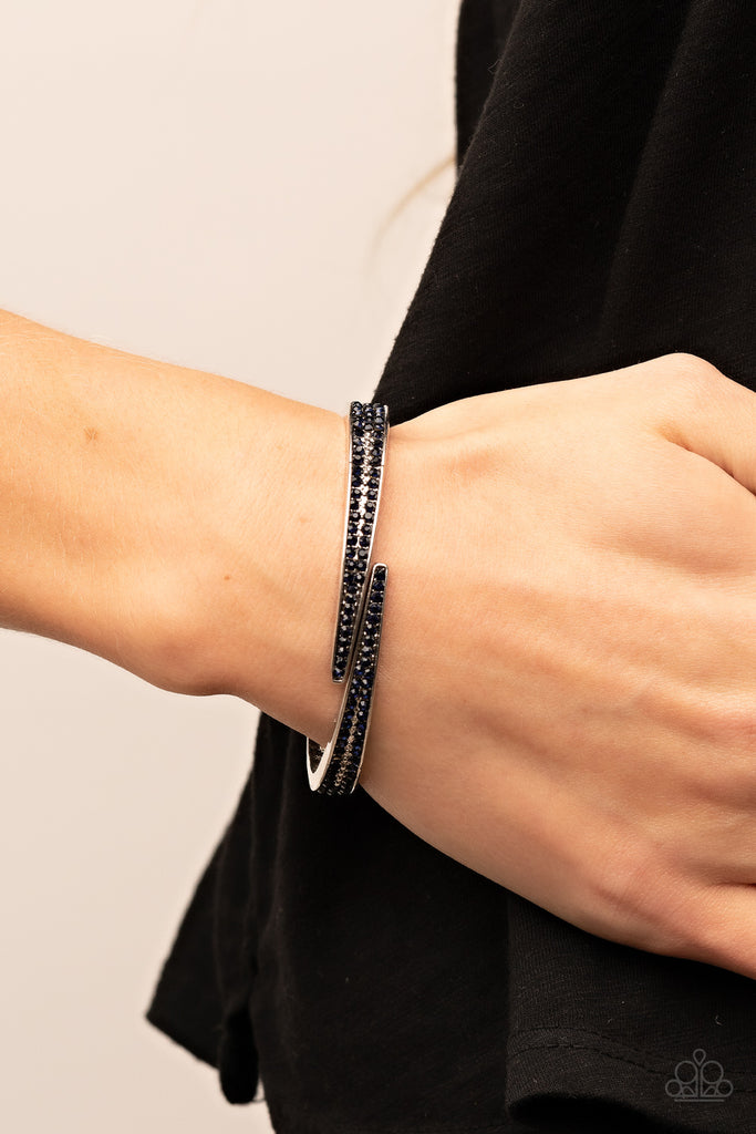 Encrusted in stacked sections of antiqued silver studs and dark blue rhinestones, two silver bars delicately overlap at the center of the wrist, resulting in an edgy cuff-like bangle. Features a hinged closure.  Sold as one individual bracelet.