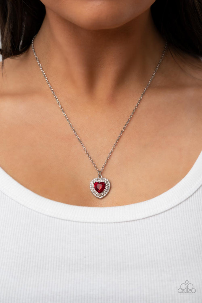 Bordered in stacked rows of glassy white rhinestones, a fiery red heart shaped gem sparkles at the center of a dainty silver chain for a flirtatious fashion. Features an adjustable clasp closure.  Sold as one individual necklace. Includes one pair of matching earrings.