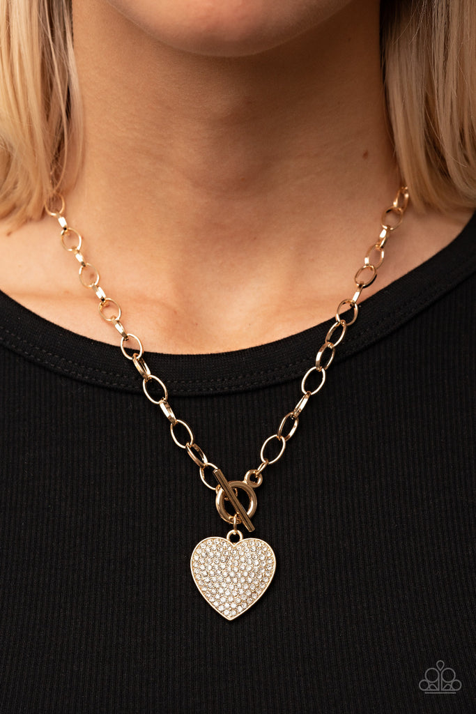A blinding white rhinestone dotted gold heart frame sparkles from a toggle closure at the center of an oval gold linked chain for a flirtatious fashion. Features a toggle closure.  Sold as one individual necklace. Includes one pair of matching earrings.