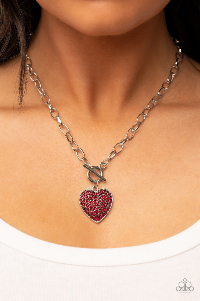 A fiery red rhinestone dotted silver heart frame sparkles from a toggle closure at the center of an oval silver linked chain for a flirtatious fashion. Features a toggle closure.  Sold as one individual necklace. Includes one pair of matching earrings.