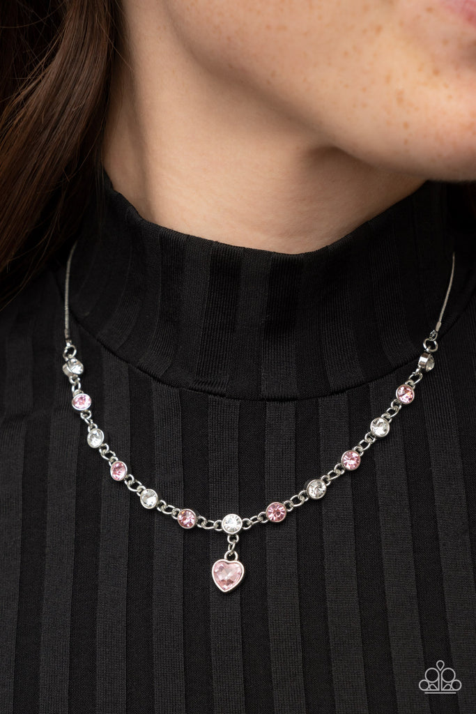 A pink rhinestone heart charm dances from a strand of white and pink rhinestones, resulting in a flirtatious sparkle below the collar. Features an adjustable clasp closure.  Sold as one individual necklace. Includes one pair of matching earrings.