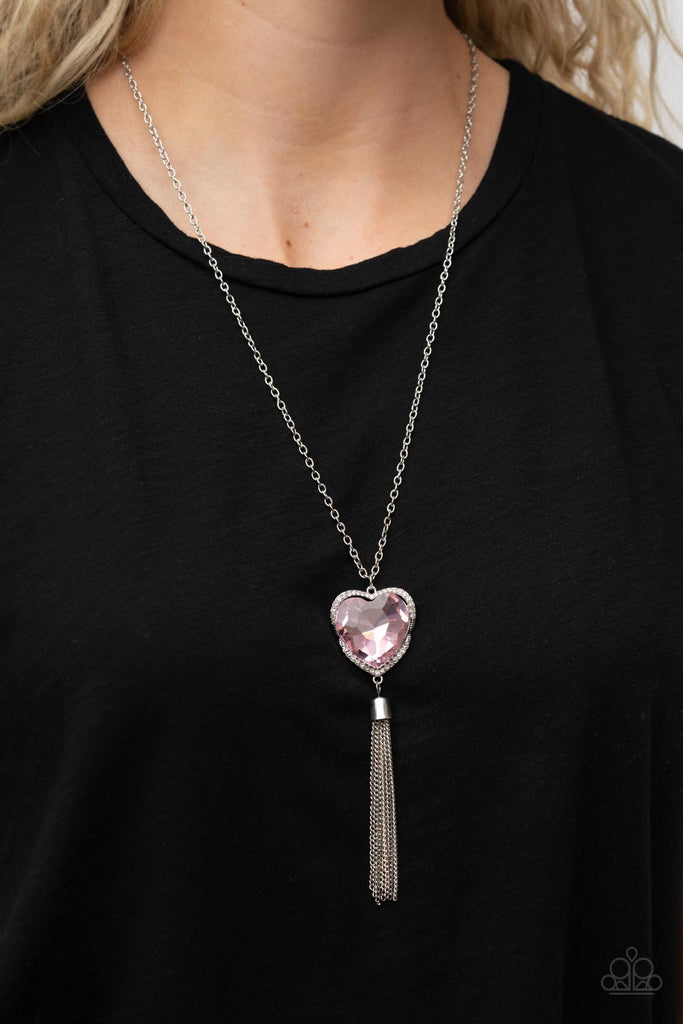 Bordered in a ribbon of glassy white rhinestones, an oversized pink heart-shaped gem seemingly floats at the bottom of an extended silver chain. A shimmery silver chain tassel dances from the bottom of the sparkly pendant for a flirtatious finish. Features an adjustable clasp closure.  Sold as one individual necklace. Includes one pair of matching earrings.