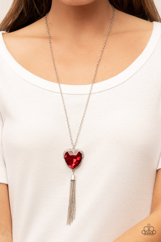 Bordered in a ribbon of glassy white rhinestones, an oversized red heart-shaped gem seemingly floats at the bottom of an extended silver chain. A shimmery silver chain tassel dances from the bottom of the sparkly pendant for a flirtatious finish. Features an adjustable clasp closure.  Sold as one individual necklace. Includes one pair of matching earrings.