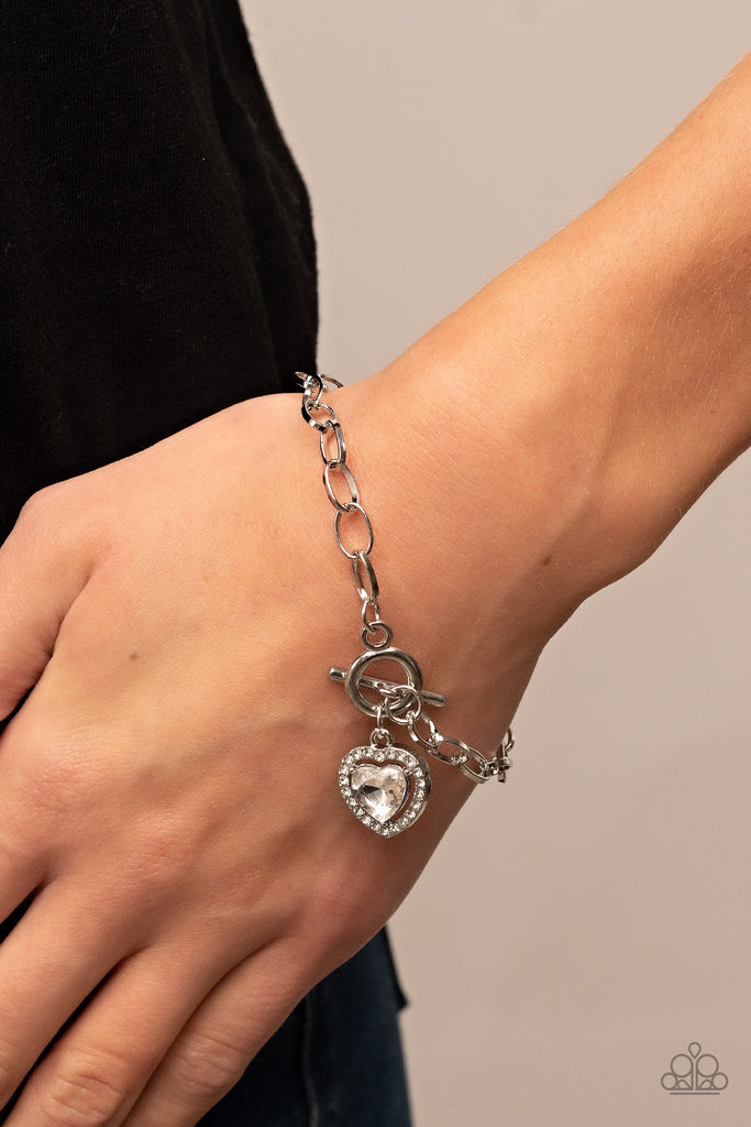 Bordered in glassy white rhinestones, a white heart shaped gem sparkles from a toggle closure at the center of an oval silver linked chain for a flirtatious fashion around the wrist. Features a toggle closure.  Sold as one individual bracelet.