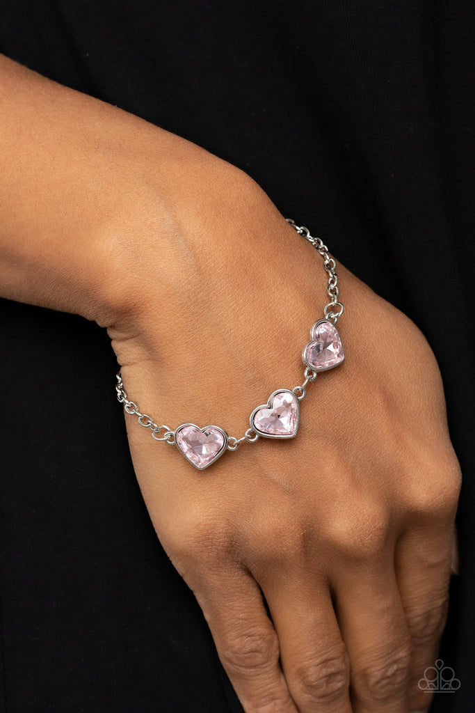 Nestled in silver frames, a trio of glittery pink heart-shaped gems delicately links across the wrist for a dash of swoon-worthy shimmer. Features an adjustable clasp closure.  Sold as one individual bracelet.