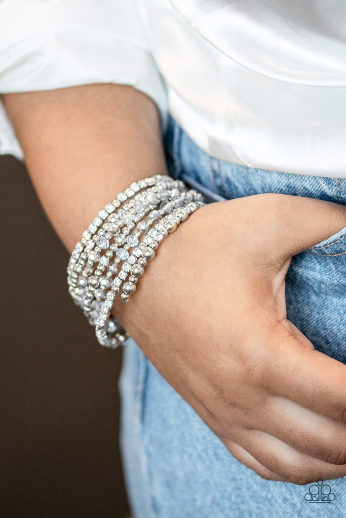 An icy collection of silver beads, silver cubes, white crystals, and glassy white rhinestones are threaded along a coiled wire, creating a blinding infinity wrap style bracelet around the wrist.  Sold as one individual bracelet.