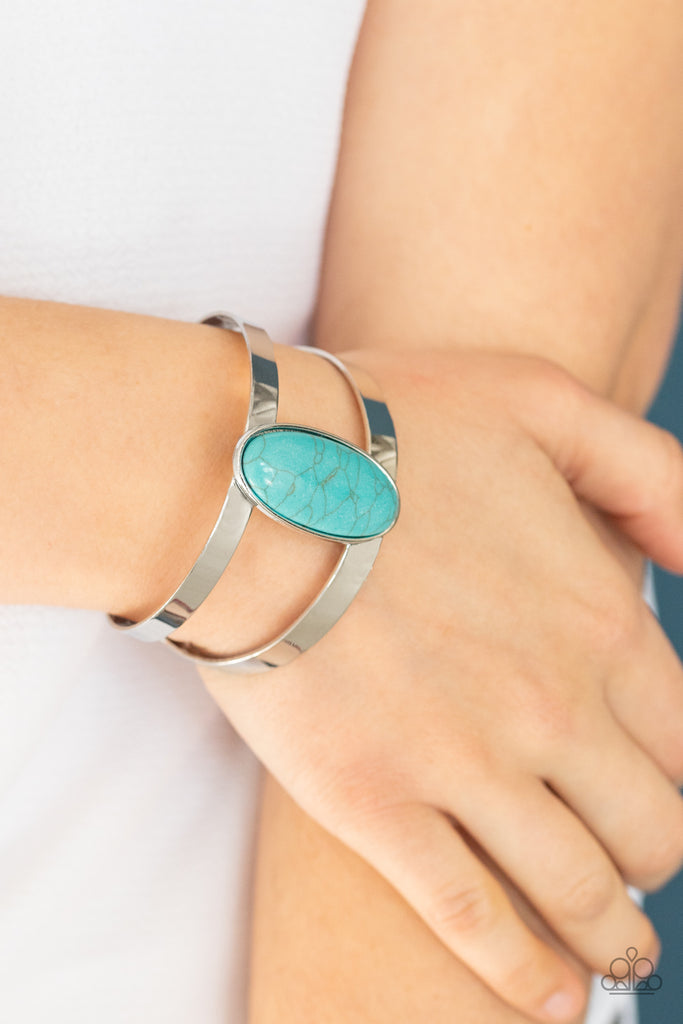 An oval turquoise stone is nestled atop the center of two shiny silver bars that curl into an airy cuff around the wrist.  Sold as one individual bracelet.