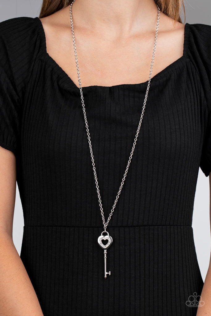 Encrusted in dainty white rhinestones, a heart-shaped silver key pendant swings from the bottom of a lengthened silver chain for a flirty look. Features an adjustable clasp closure.  Sold as one individual necklace. Includes one pair of matching earrings.