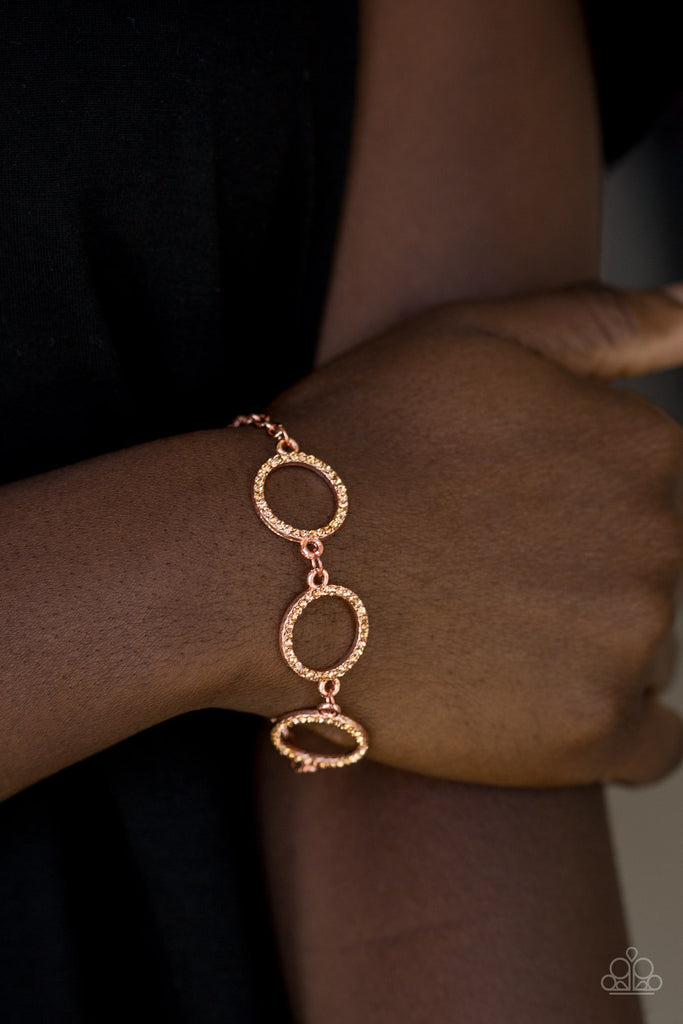 Encrusted in peachy colored rhinestones, three glittery shiny copper rings link across the wrist for a glamorous look. Features an adjustable clasp closure.  Sold as one individual bracelet.
