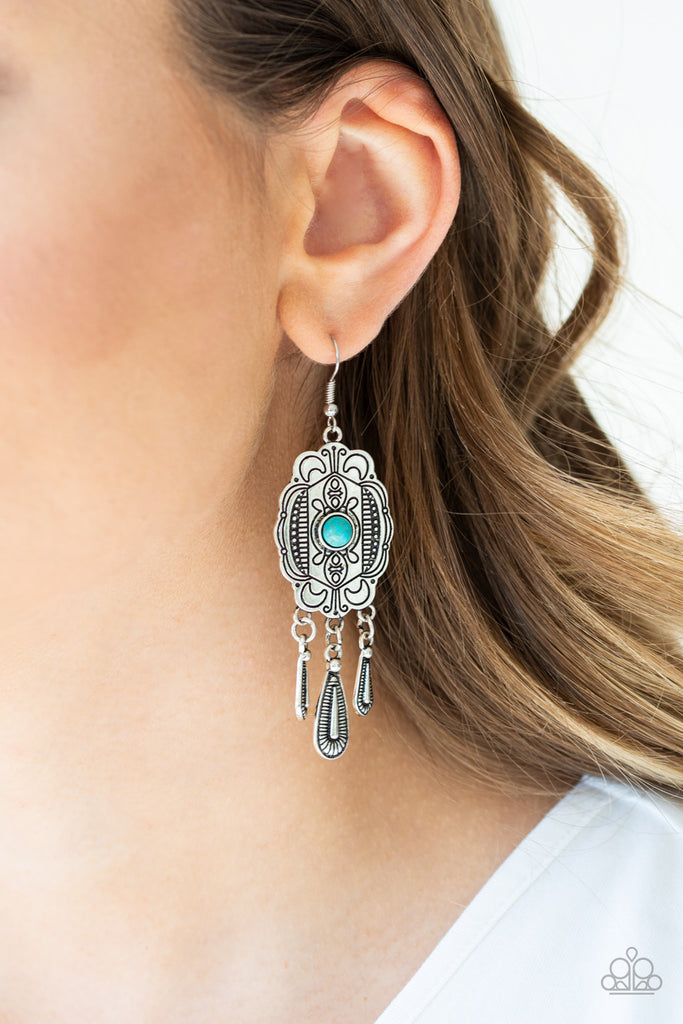 A dainty blue stone bead is pressed into the center of an antiqued silver frame stamped in tribal inspired patterns. Textured silver teardrops swing from the bottom of the frame, creating a whimsical fringe. Earring attaches to a standard fishhook fitting.  Sold as one pair of earrings.