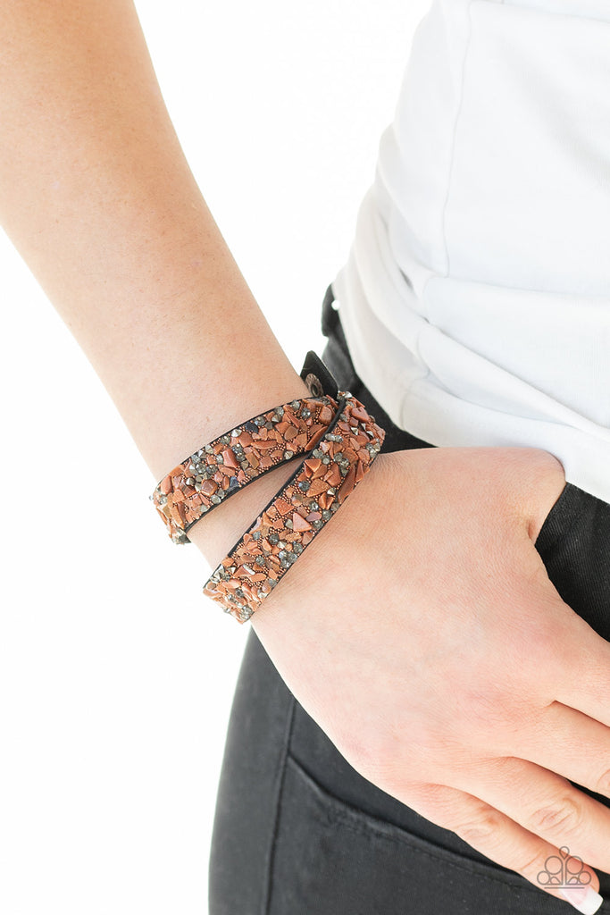 A collection of crushed brown rocks, smoky and hematite rhinestone prisms are sprinkled across a black suede band for a seasonal look. The elongated band allows for a trendy double wrap design. Features an adjustable snap closure.  Sold as one individual bracelet.