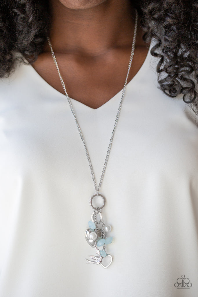 A silver bird charm, silver heart charms, and collection of white pearls and opaque blue crystal-like beads swing from the bottom of a lengthened silver chain for a whimsically clustered look. Features an adjustable clasp closure.  Sold as one individual necklace. Includes one pair of matching earrings.
