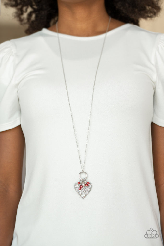 Infused with dainty red pearls and a shimmery silver heart charm, a stenciled silver heart pendant swings from the bottom of a lengthened silver chain for a whimsical look. Features an adjustable clasp closure.  Sold as one individual necklace. Includes one pair of matching earrings.