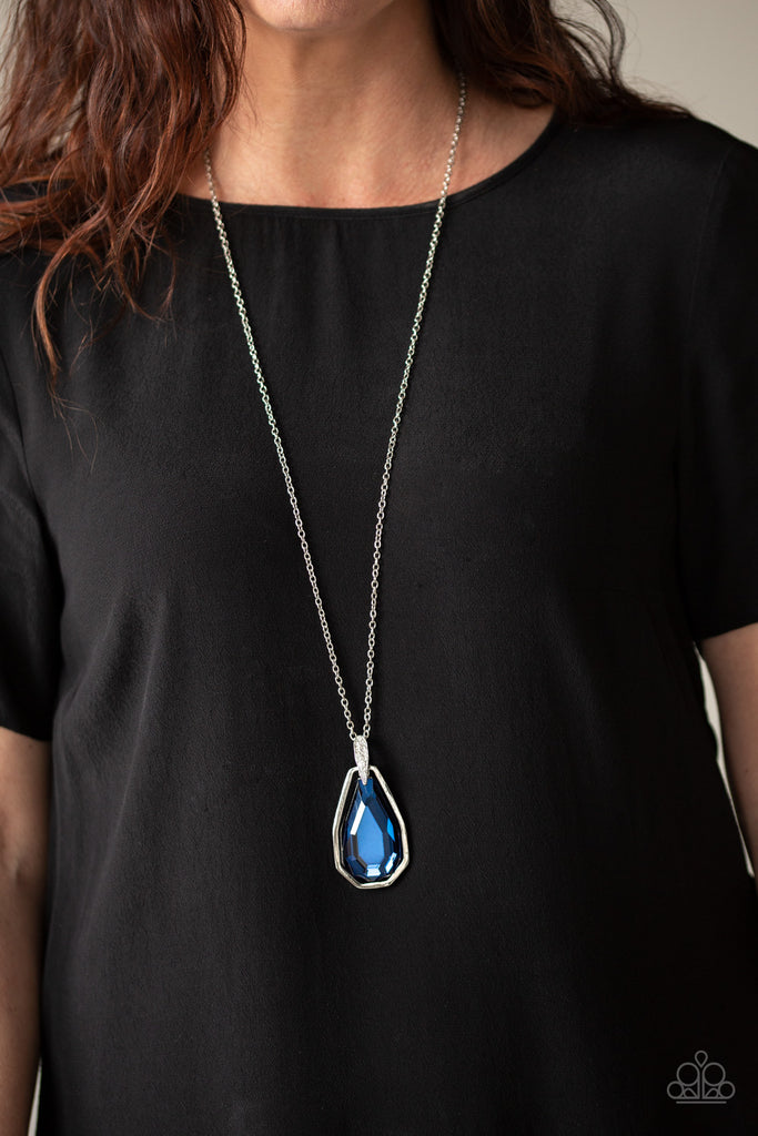 A dramatically over sized blue gem and edgy silver frame swing from a glassy white rhinestone fitting at the bottom of a lengthened silver chain for a glamorous look. Features an adjustable clasp closure.  Sold as one individual necklace. Includes one pair of matching earrings.