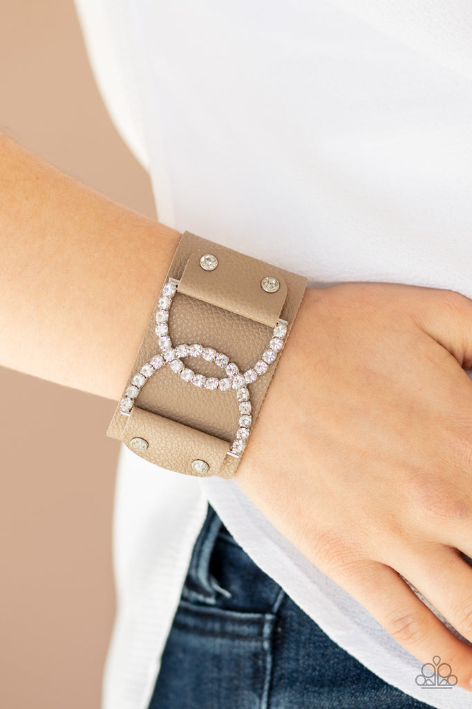 Encrusted in glassy white rhinestones, two interlocking half moon silver frames are studded in place across the front of a brown leather band for a statement-making finish. Features an adjustable snap closure.  Sold as one individual bracelet.