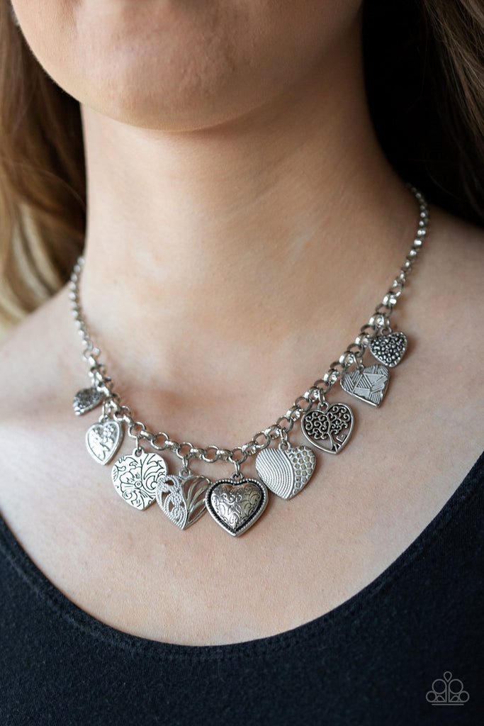 Featuring an array of floral patterns, a collection of silver hearts swing from the bottom of a shimmery silver chain. Alternating charms are brushed in a shiny white finish, creating a colorful fringe below the collar. Features an adjustable clasp closure.  Sold as one individual necklace. Includes one pair of matching earrings.