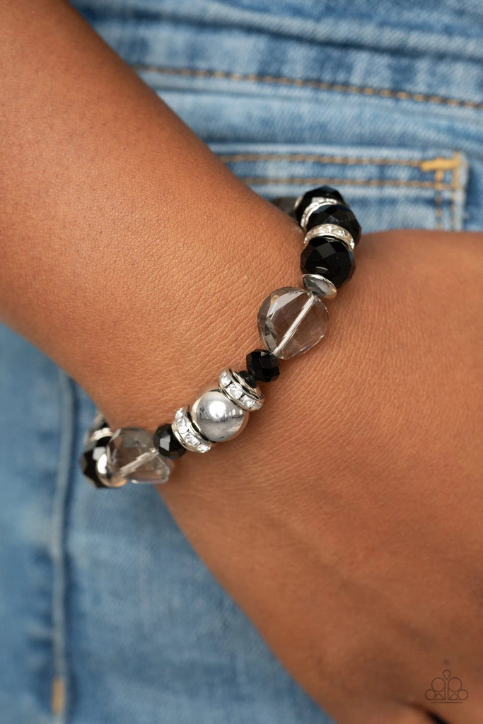 A glamorous collection of white rhinestone encrusted rings, silver beads, glassy white gems, and glittery black crystal-like beads are threaded along a stretchy band around the wrist for a refined flair.  Sold as one individual bracelet.
