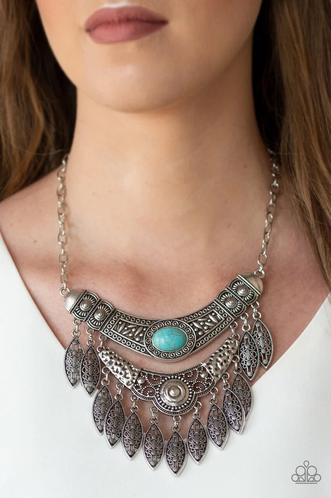 Featuring a collision of hammered, studded, and embossed patterns, two silver half-moon plates dramatically stack below the collar. Swirling with studded filigree detail, ornate silver frames swing from the bottoms of the stacked pendants, creating a fierce tribal inspired fringe. A refreshing turquoise stone is pressed into the center of the uppermost frame for a seasonal finish. Features an adjustable clasp closure.  Sold as one individual necklace. Includes one pair of matching earrings.
