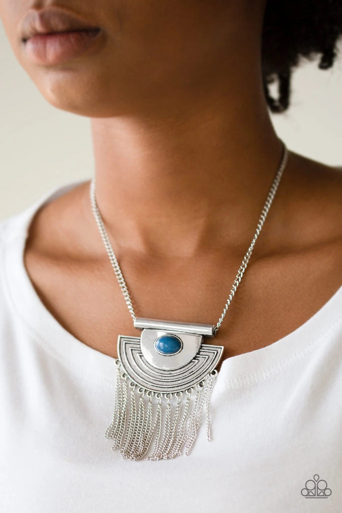 A refreshing blue bead is pressed into the center of an antiqued silver crescent shaped pendant radiating with geometric patterns. Antiqued silver tassels swing from the bottom of a bold pendant, creating a fierce fringe below the collar. Features an adjustable clasp closure.  Sold as one individual necklace. Includes one pair of matching earrings.