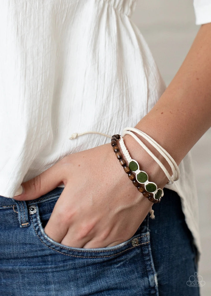 Mismatched strands of white cording, brown wooden beads, and knotted white twine knotted around earthy Military Olive wooden accents delicately layer across the wrist for a colorful look. Features an adjustable sliding knot closure.  Sold as one individual bracelet.