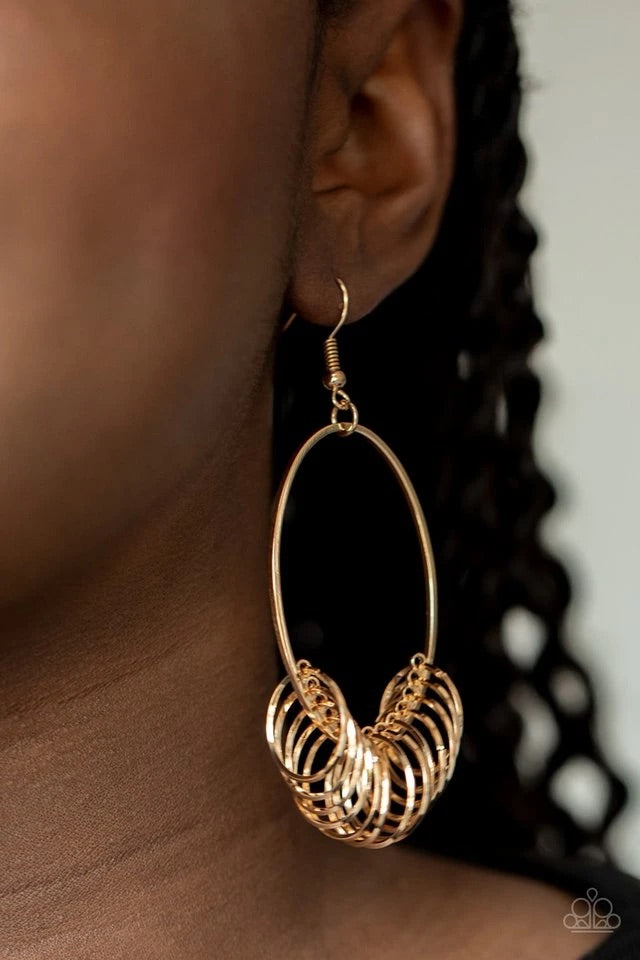 A collection of dainty gold rings are secured in place along the bottom of a gold oval frame, creating a dizzying fringe. Earring attaches to a standard fishhook fitting.  Sold as one pair of earrings.  