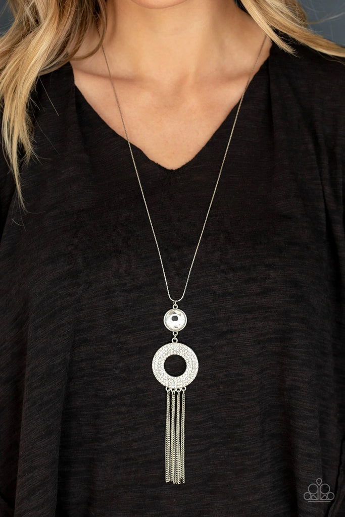 An oversized white gem attaches to a thick silver hoop encrusted in row after row of dazzling white rhinestones. Shimmery silver chains stream from the bottom of the stacked pendant at the bottom of a lengthened flat silver chain, creating a sassy tassel. Features an adjustable clasp closure.  Sold as one individual necklace. Includes one pair of matching earrings.