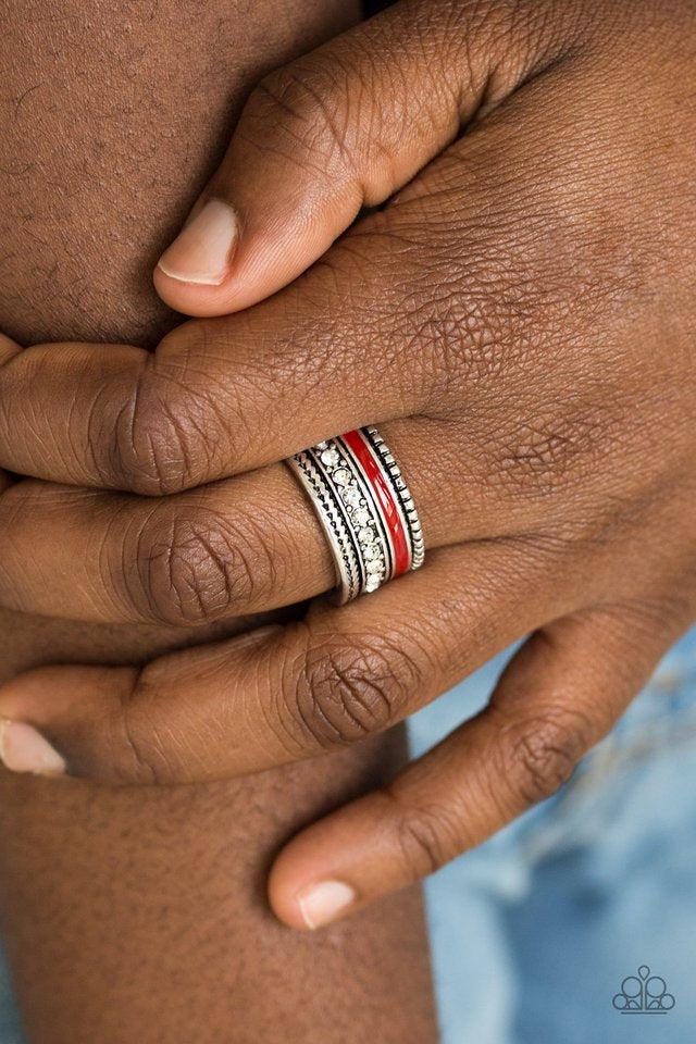 A shiny red strip of color runs along the bottom of a row of glassy white rhinestones. Infused with silver textures, the mismatched details coalesce into one thick band across the finger. Features a stretchy band for a flexible fit. Sold as one individual ring.