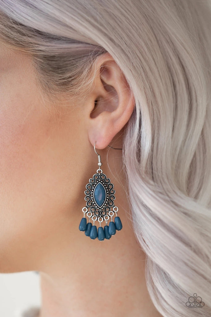 A faceted blue bead is pressed into the center of a studded silver frame radiating with antiqued filigree. Matching blue beads swing from the bottom of the frame, creating a whimsical fringe. Earring attaches to a standard fishhook fitting.  Sold as one pair of earrings.