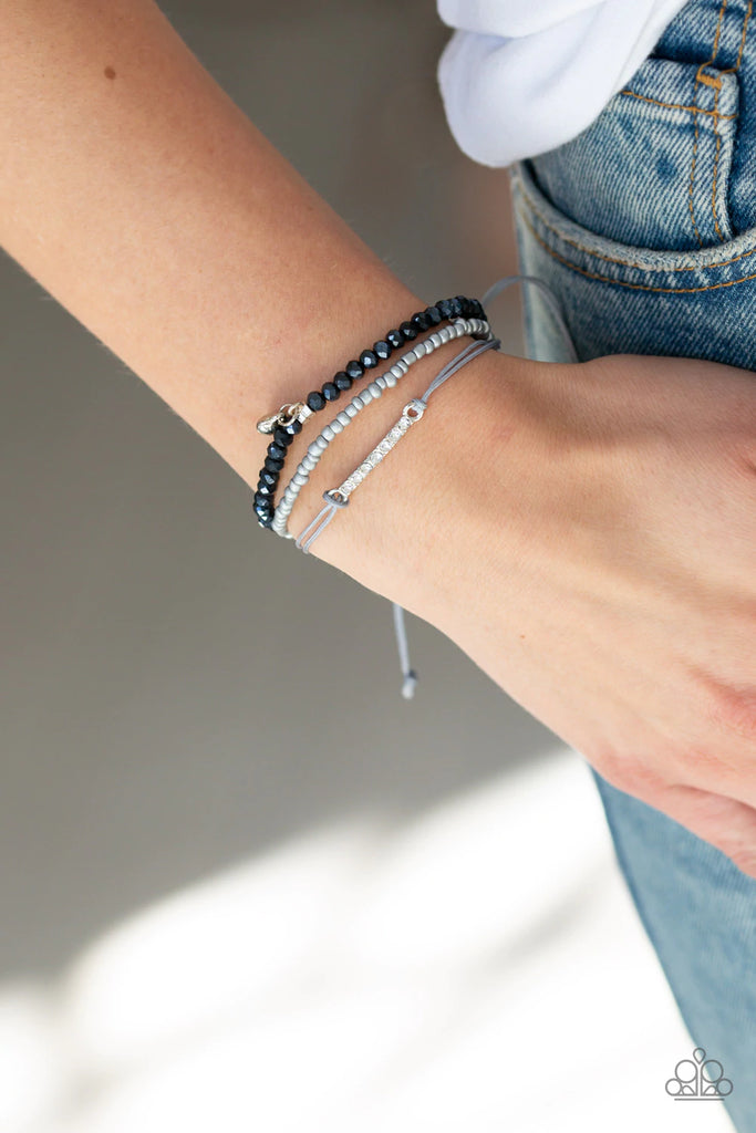 Brushed in an iridescent shimmer, a row of faceted metallic blue beads and a strand of glistening metallic seed beads layer across the wrist. Featuring a rhinestone encrusted frame, a strand of gray cording is added to the layers, while a silver heart charm swings from the wrist for a whimsical finish. Features an adjustable sliding knot closure.  Sold as one individual bracelet.  