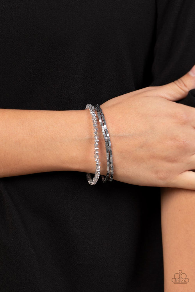Two rows of dainty silver cube beads and one row of smoky crystal-like beads are threaded along stretchy bands around the wrist, creating stellar layers.  Sold as one set of three bracelets.