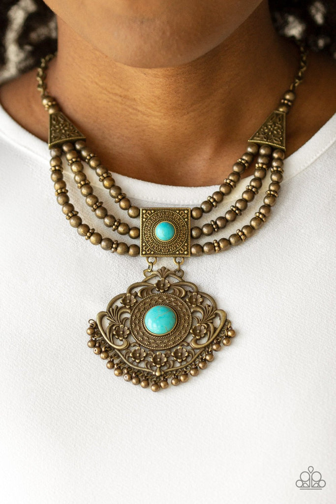Dotted with refreshing turquoise stone centers, two ornate frames link below the collar. Strands of brass beads are threaded through the uppermost pendant, adding an antiqued flair to the tribal inspired pendant. Features an adjustable clasp closure.  Sold as one individual necklace. Includes one pair of matching earrings.