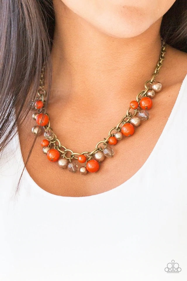 Pearly brass, polished orange, and glittery crystal-like beads swing from a bold brass chain, creating a refined fringe below the collar. Features an adjustable clasp closure. Sold as one individual necklace. Includes one pair of matching earrings.