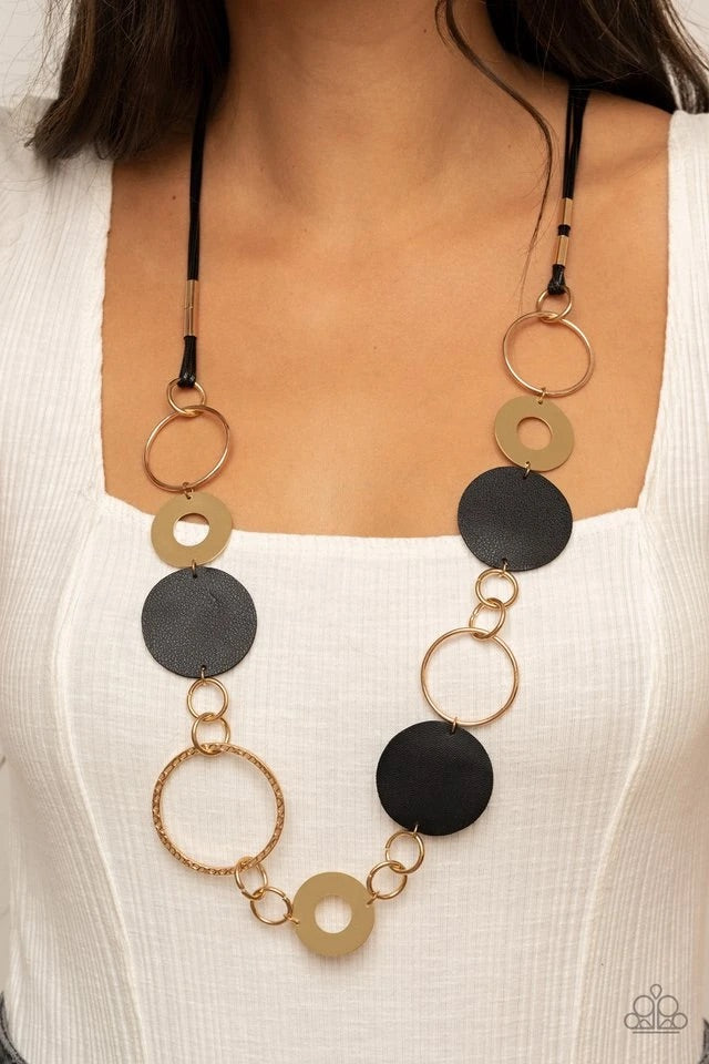A shiny collection of mismatched gold rings and textured hoops link with round pieces of black leather across the chest for a whimsically retro look. The colorful compilation attaches to layered strands of shiny black cording for a trendy finish. Features an adjustable clasp closure.  Sold as one individual necklace. Includes one pair of matching earrings.