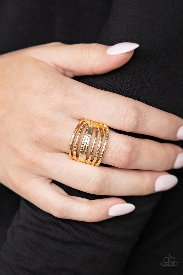 A collection of smooth and textured gold bars arc across the finger, stacking into a thick layered band. Features a stretchy band for a flexible fit.  Sold as one individual ring.