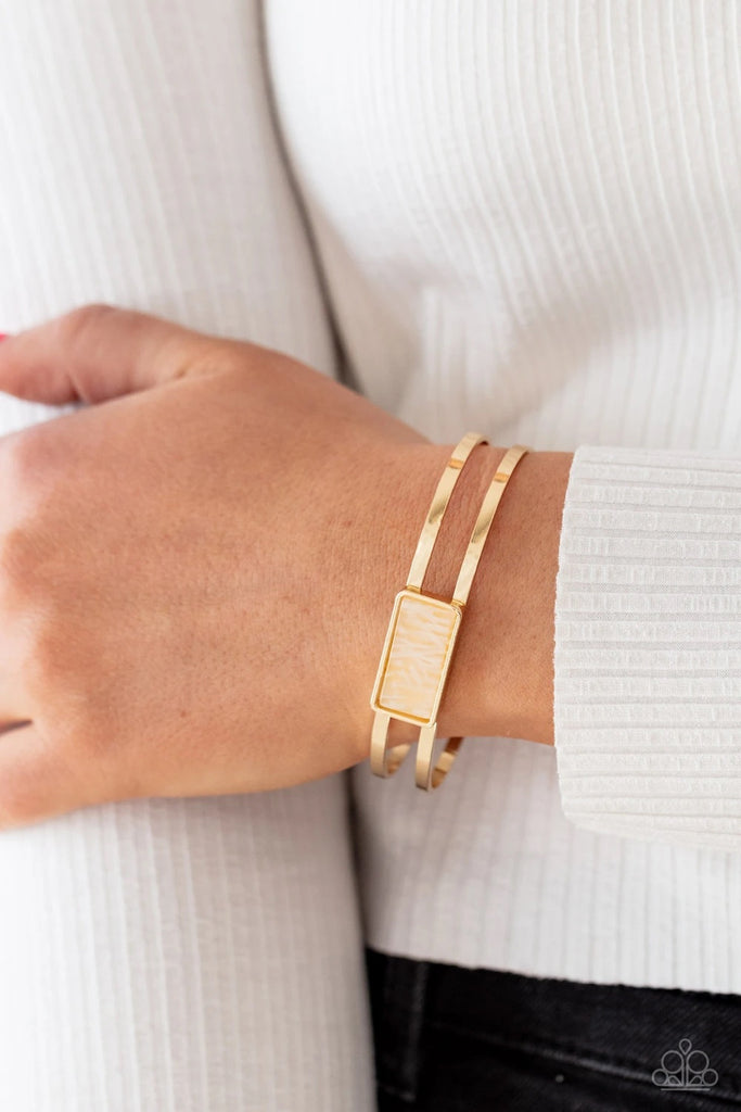 A bold shell-like acrylic accent is encased in a shiny gold rectangular frame which sits resolutely atop a double-bar gold cuff. Color and pattern may vary.  Sold as one individual bracelet.