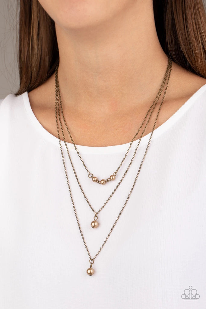 A trio of pearly brass beads give way to layers of solitaire brass pearl pendants below the collar for a refined flair. Features an adjustable clasp closure.  Sold as one individual necklace. Includes one pair of matching earrings.