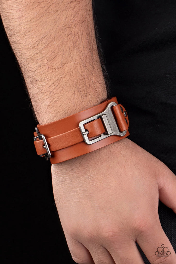A collection of leather pieces and antiqued gunmetal frames are studded in place across the front of a thick leather band, creating an abstract buckle. Features an adjustable snap closure.  Sold as one individual bracelet.