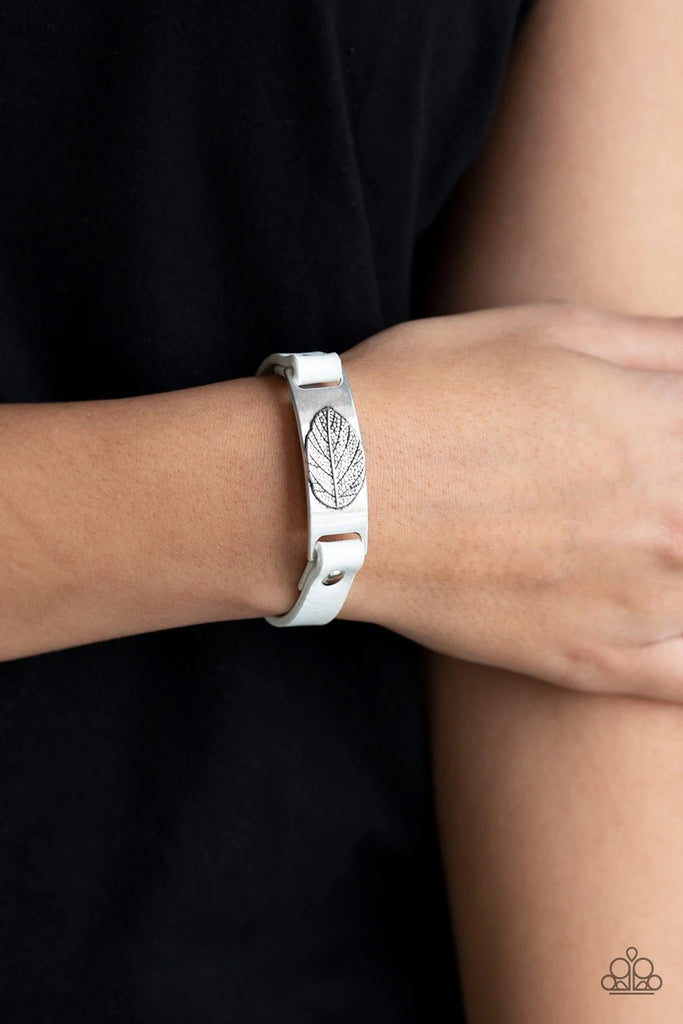 Brushed in an antiqued finish, a life-like leaf is embossed in the center of a silver plate. White leather bands loop through the silver centerpiece and are studded in place across the wrist for a seasonal look. Features an adjustable snap closure.  Sold as one individual bracelet.