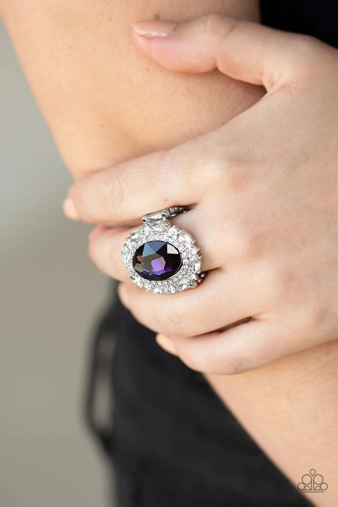 An oversized oval purple gem is pressed into the center of a round silver frame encrusted in mismatched white rhinestones for a glamorous look. Features a stretchy band for a flexible fit.  Sold as one individual ring.
