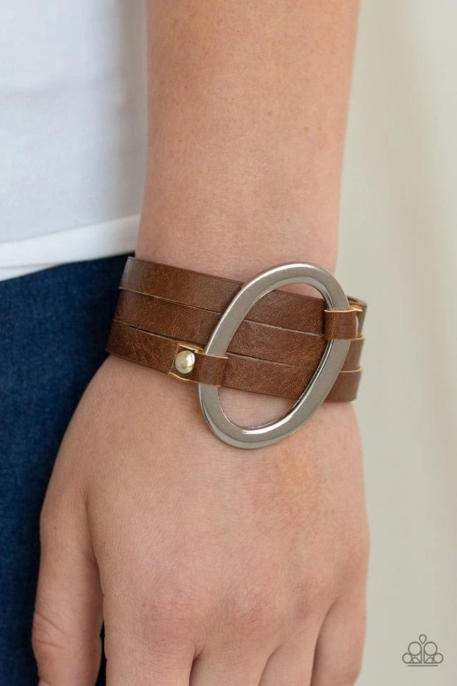 An oval silver ring loops through two belt loop fittings and is studded in place across the front of a spliced brown leather band for a bold urban look. Features an adjustable snap closure. Sold as one individual bracelet.